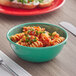 A bowl of pasta with green sauce and parsley in a green Acopa melamine nappie bowl on a table.