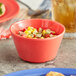 An Acopa orange melamine bouillon bowl filled with food on a table.