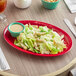 A red Acopa Foundations melamine oval platter with salad on a table.