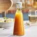 A Tablecraft glass carafe filled with orange sauce on a table.