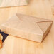 A brown Fold-Pak Sonoma paper take-out box on a table with a croissant inside.