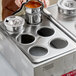 A woman using a ServIt steam table adapter plate with holes to pour liquid into a pot.