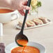 A person using a Tablecraft black silicone-coated stainless steel ladle to pour soup into a bowl.