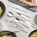 A table with silverware, including Acopa Heika steak knives, and plates of food.