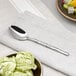 An Acopa stainless steel teaspoon on a table next to a bowl of green ice cream.