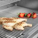 A Crown Verity built-in grill with chicken legs and peppers cooking on it.