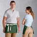 A man and woman wearing Choice hunter green waist aprons with natural webbing.