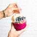 A person holding a bowl of Pitaya Foods Dragon Fruit Sorbet topped with fruit