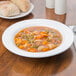 An Arcoroc Zenix glass bowl of soup on a wood table.