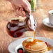 A hand using a Vollrath syrup dispenser to pour syrup on pancakes on a table.