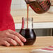 A hand pouring brown syrup from a Vollrath Teardrop syrup server into a glass.