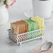 A Vollrath rectangular chrome sugar caddy holding packets of sugar on a counter.