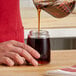 A person pouring brown liquid from a Vollrath glass syrup server.