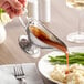 A person using a Vollrath stainless steel gravy boat to pour gravy over mashed potatoes.