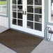 A brown Lavex Chevron Rib indoor entrance mat with double glass doors.