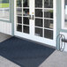 A blue Lavex Chevron Rib entrance mat in front of double doors with glass panes.