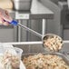 A hand holding a blue Choice 8 oz. portion spoon over a plastic container of food.