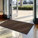 A brown Lavex Needle Rib carpet mat in front of a building's glass doors.