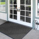 A black Lavex Chevron Rib indoor entrance mat on a white door.