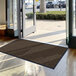 A brown Lavex Needle Rib entrance mat in front of a large glass door.