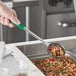 A hand holding a Choice green solid portion spoon over a food container.