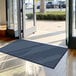 A blue Lavex Needle Rib indoor entrance mat in front of a large glass door.