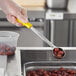A person in a glove holding a Choice yellow perforated portion spoon of olives.
