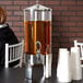 A woman sitting at a white table with a Vollrath beverage dispenser on it.