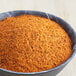 A bowl of red and yellow ground McCormick Rotisserie Chicken Seasoning on a table.