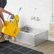 A man using a yellow mop to clean a Regency stainless steel floor mop sink.