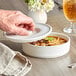 A hand holding a white Tuxton Tortilla Server over a bowl of food.