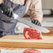 A person cutting meat with a Choice 12" Butcher Knife on a wooden cutting board.