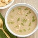 A bowl of Campbell's cream of potato soup with a spoon and green sprig, with crackers on a plate.