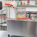 A person using a wire basket to fry food in a Cecilware countertop deep fryer.