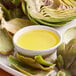 A bowl of clarified butter next to artichokes.
