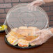 A plastic gloved hand holding a Sabert clear plastic lid on a container of food.