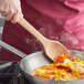 A person stirring vegetables in a skillet with an OXO wooden corner spoon.