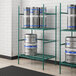 A Regency green metal shelf with kegs on it.