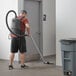 A man using a Hoover HVRPWR cordless backpack vacuum cleaner to vacuum the floor of a room.