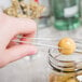 A person using Fineline clear plastic tongs to pick up a round object.