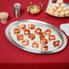 A Vollrath stainless steel oval fluted tray with food on a table.
