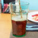 A person pouring brown soda into a Cambro Spanish Green plastic tumbler.