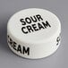 A white round silicone lid with black text that reads "Sour Cream"