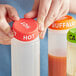 A person using a white Choice "Hot" silicone lid to cover a bottle of hot sauce.