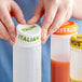 A hand using a white silicone lid to cover a plastic bottle filled with different colored liquids.