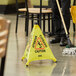 A person holding a broom and sweeping near a yellow Lavex Caution Wet Floor sign.