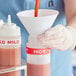 A hand using a red silicone band to pour hot liquid into a bottle.