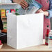 A person in an apron putting a white Choice paper bag into another white Choice paper bag.
