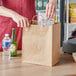 A hand holding a Choice natural kraft paper bag with food inside.