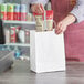 A person's hand putting food in a white Choice shopping bag.